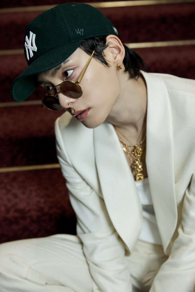 JUNHEE Supernova teaser; he has a dark green baseball cap, golden jewelery and sunglasses, and an all-white casual suit.