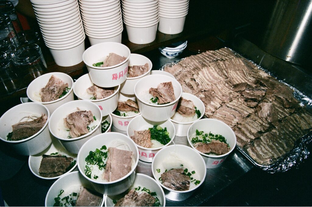 Table filled with bowls of pho and a tray of briskets.