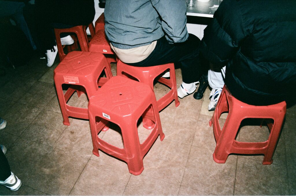 Five red chairs with no backrests, two of them are filled.