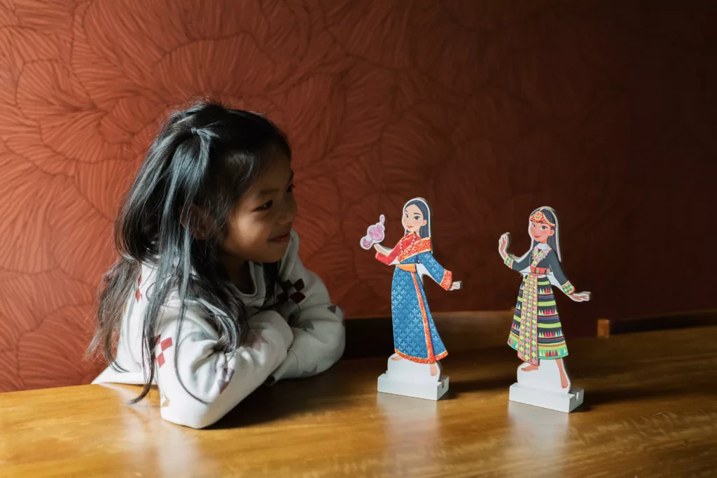 A girl looking lovingly at two Stay Curious Toys paper dolls. 