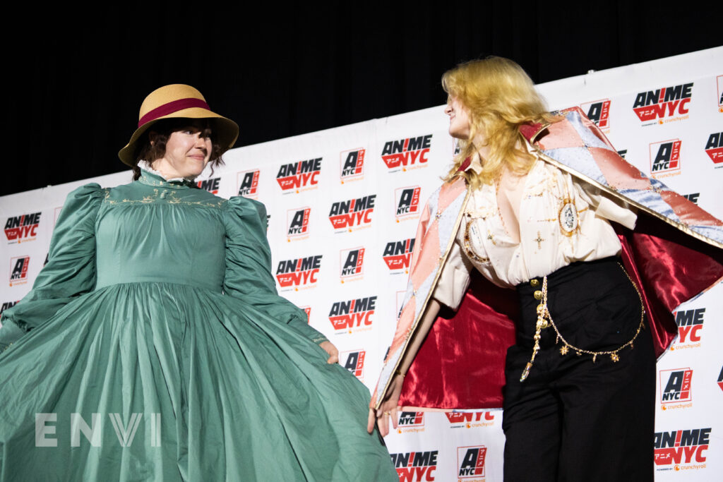 Two cosplayers dressed as Howl and Sophie from Howl's Moving Castle look towards each other with warm smiles