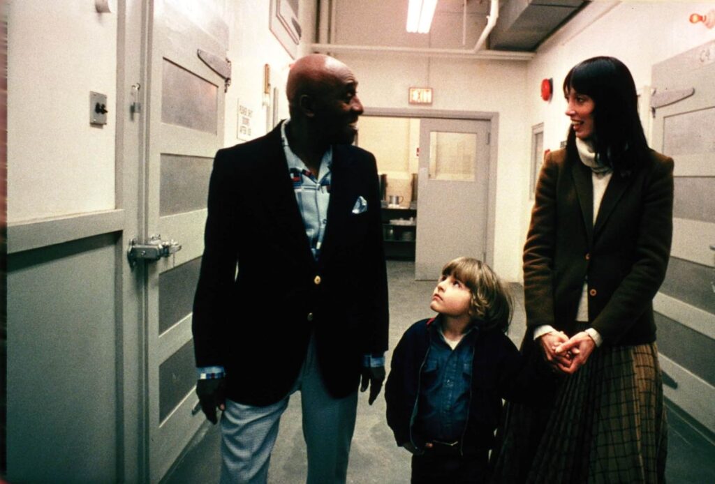 A man stands with a young child and woman in the hallway of a building. They are in the middle of conversation