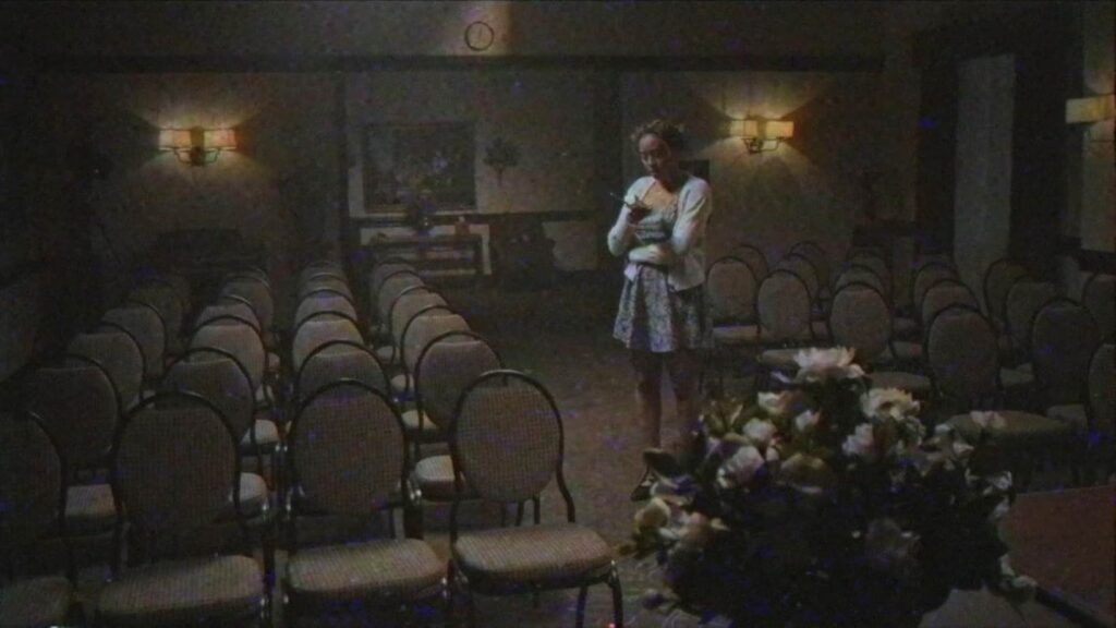 A Young woman wearing white and blue stands in a room of empty chairs