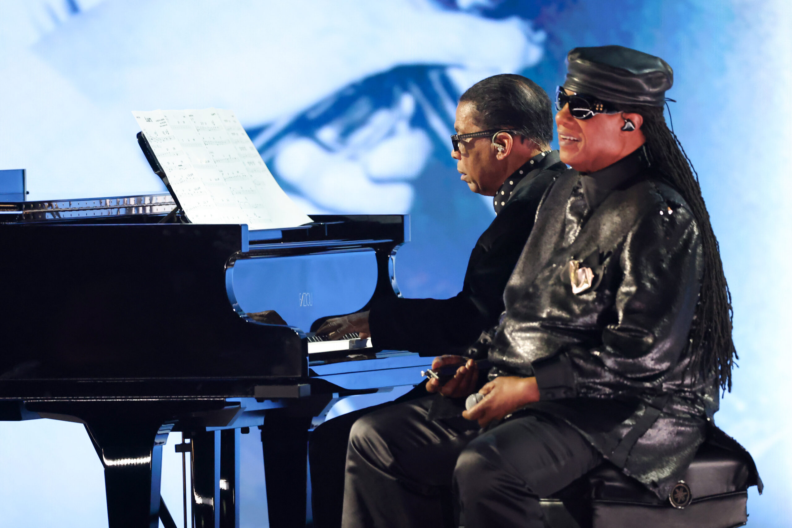 Herbie Hancock and Stevie Wonder perform on stage at the 67th annual Grammys. The two sit on stage by a Piano.