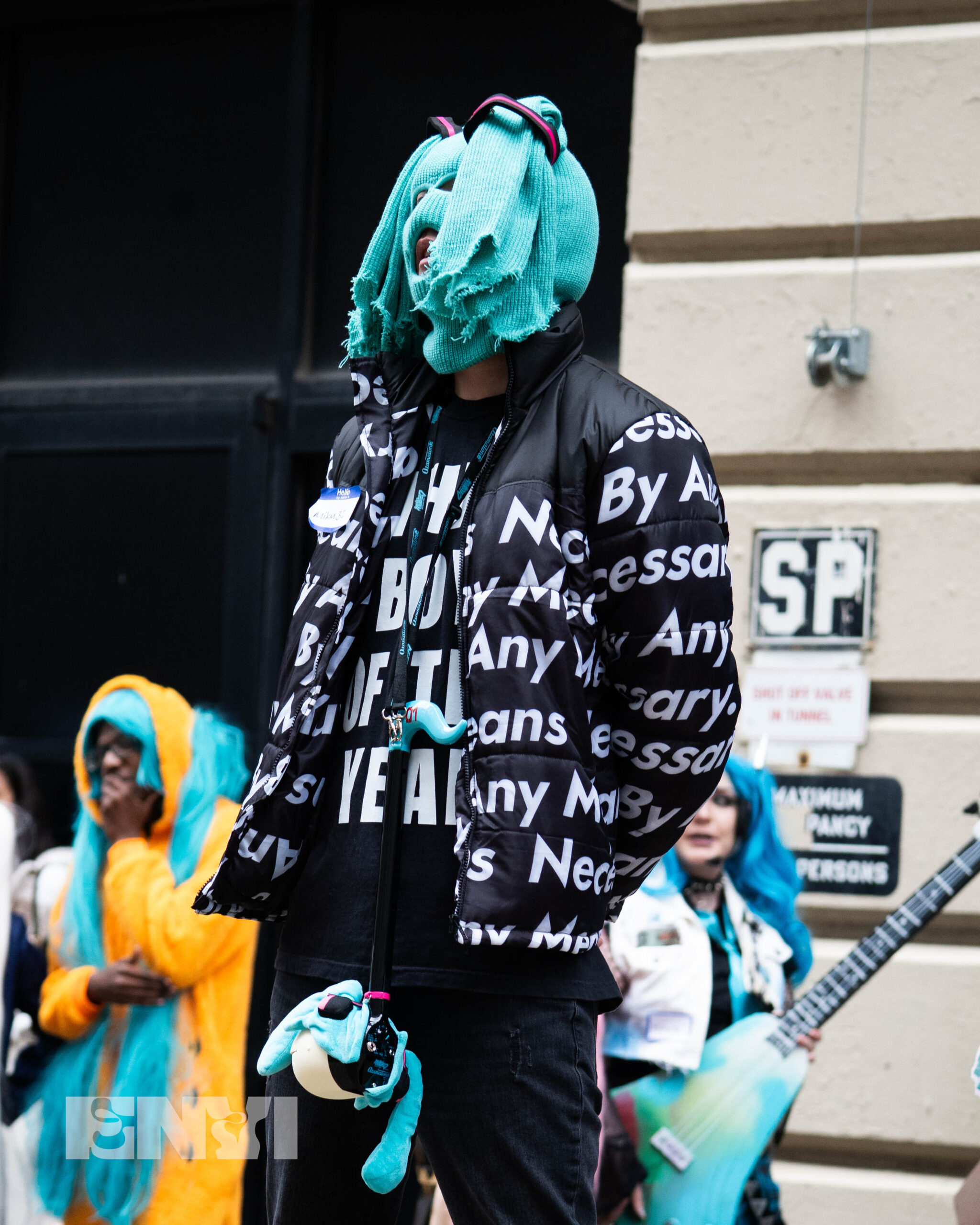 A competitor dressed up as an alternative universe version of Hatsune Miku based off of a popular meme. On his head is a Blue ski mask fitted to mimic two Pigtails and a black and white Supreme Jacket.