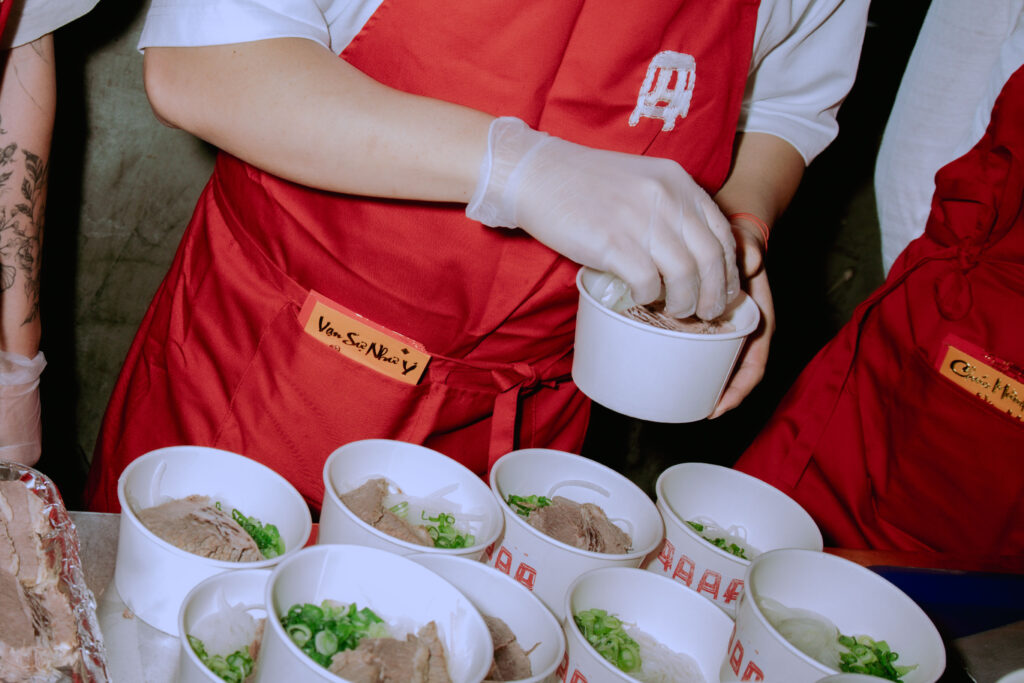 A zoomed in hand of a person adding condiments to a bowl of pho.