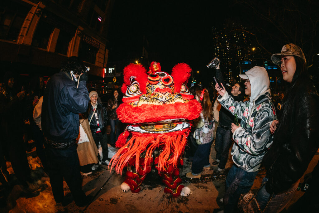 A fisheye lens view of a red lion dancer surroudned by multiple people watching them.