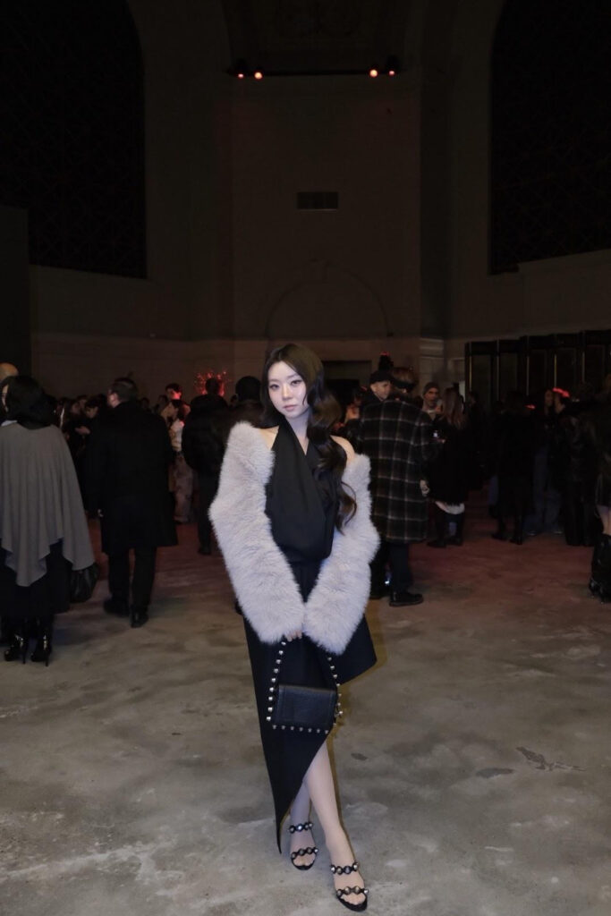 Sujin Gwon posing with a black dress and white fur cardigan.