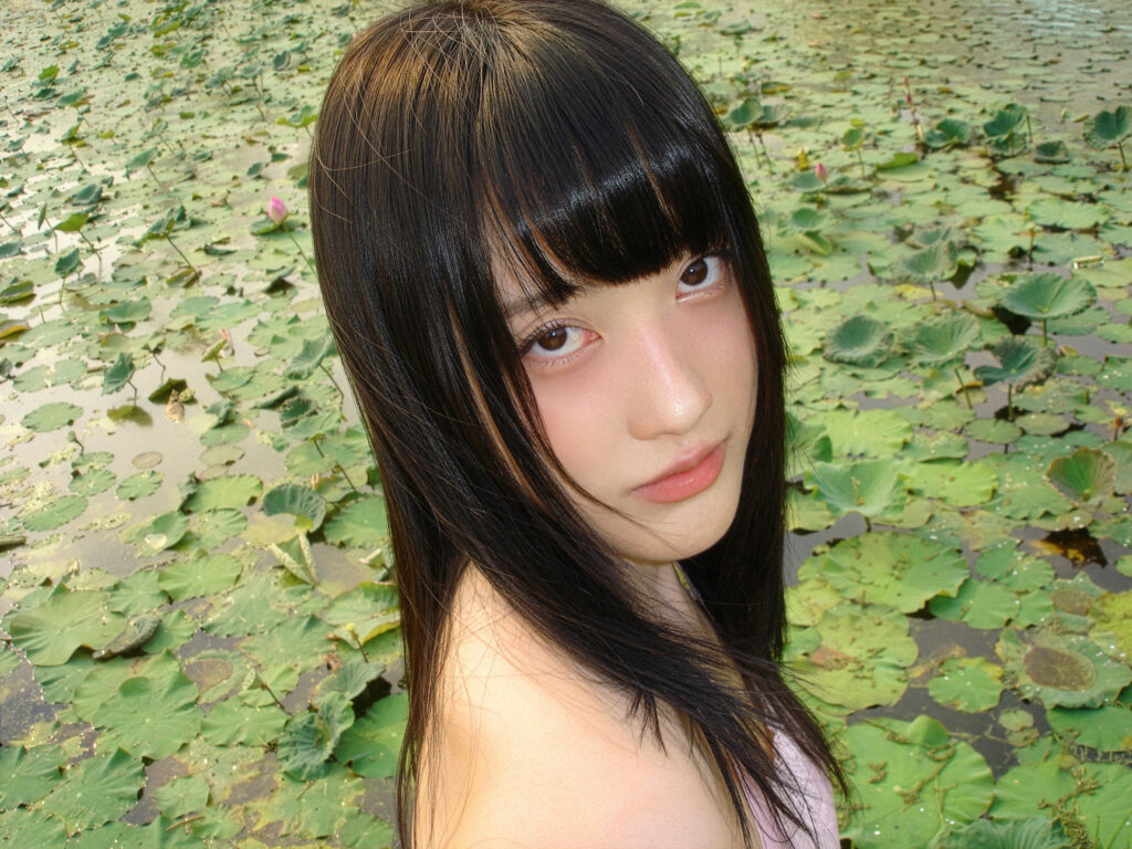 close up pami standing against a pond filled with lotus pads.