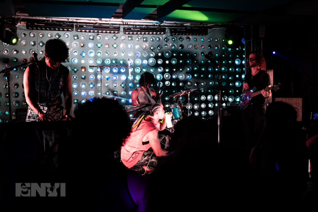 Ian Ackerman engages in a guitar solo while RUOK and Danny Singh are on stage. Singh, bends down while looking at the guitarist. 