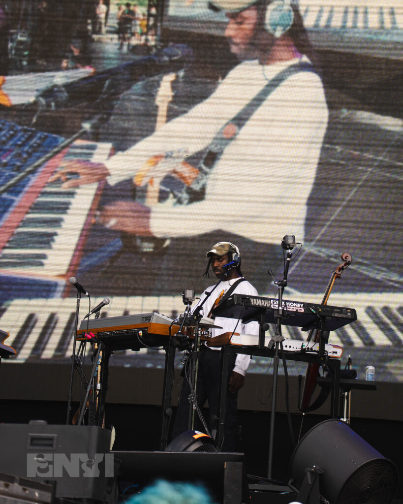 Blood Orange, a Black man in a white shirt plays several keyboards on a stage.